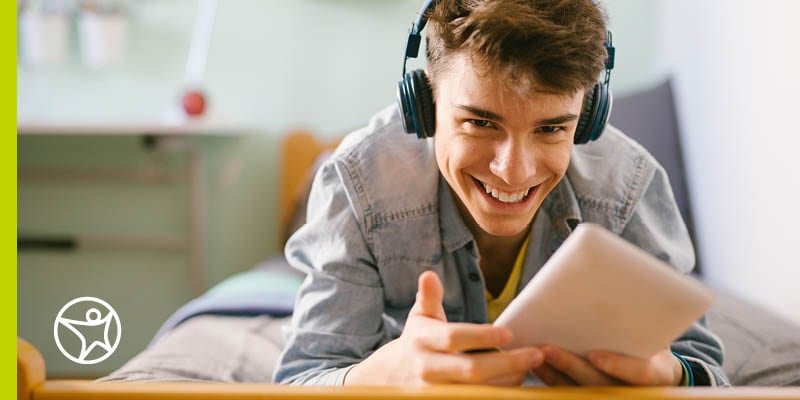 A teenager is smiling and listening to headphones on his bed