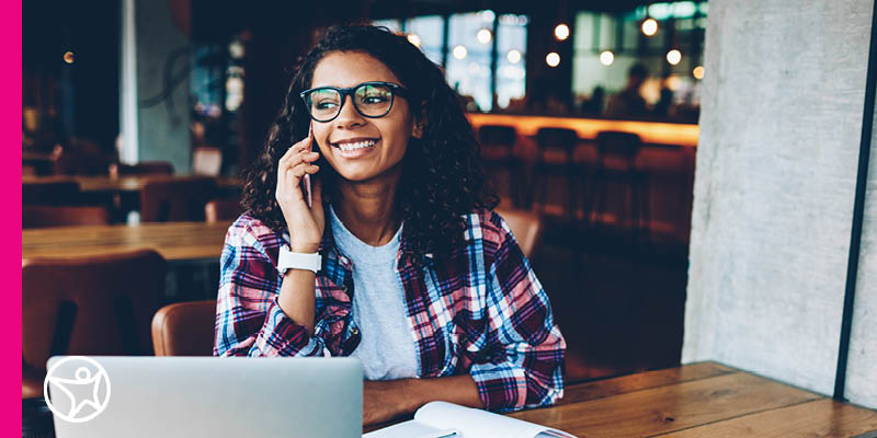 A woman sitting at a desk working on a laptop and speaking to someone on the phone
